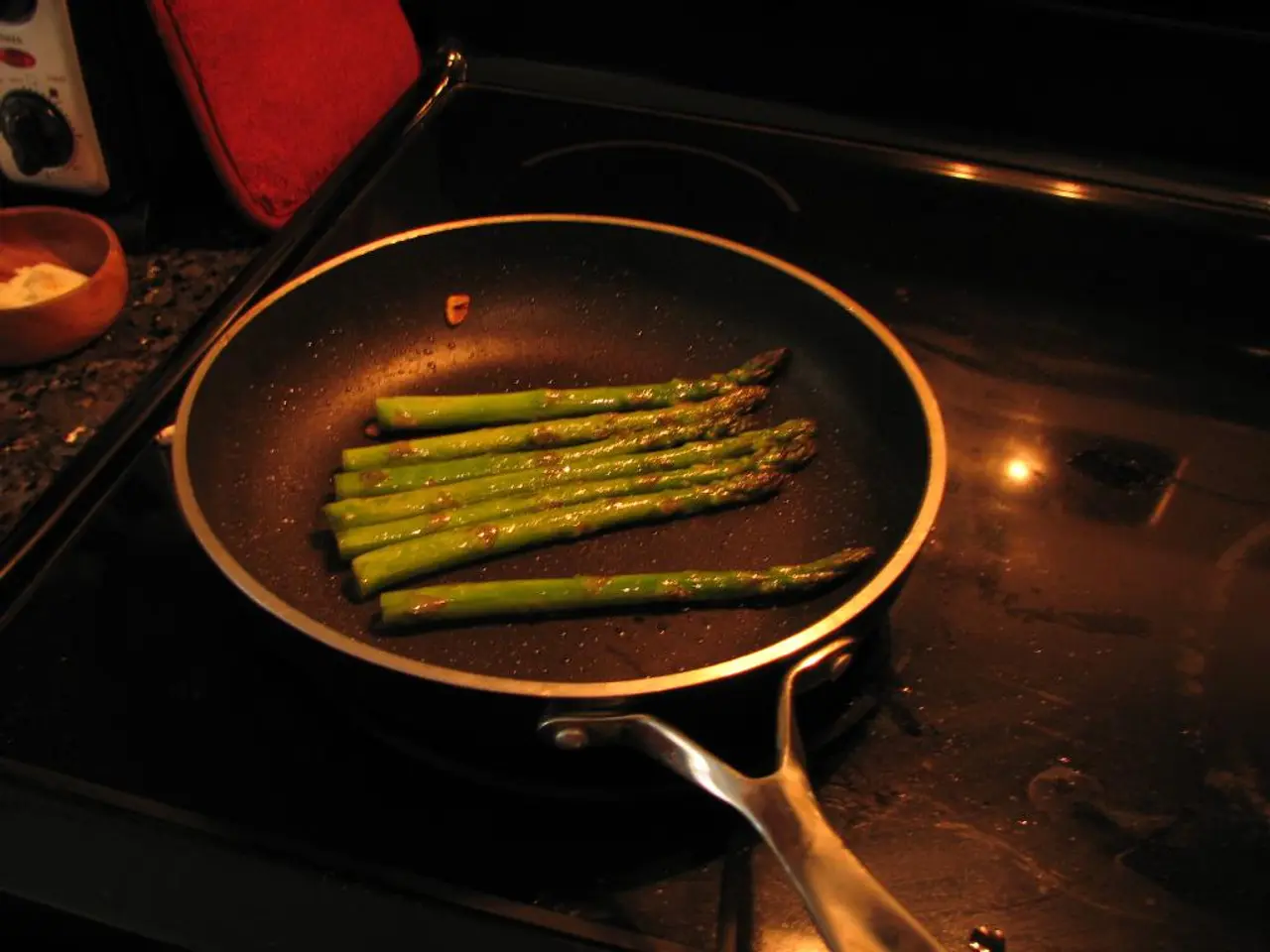 There is a pan on the stove. On the pan there is a food item. On the left side there is a bowl with...