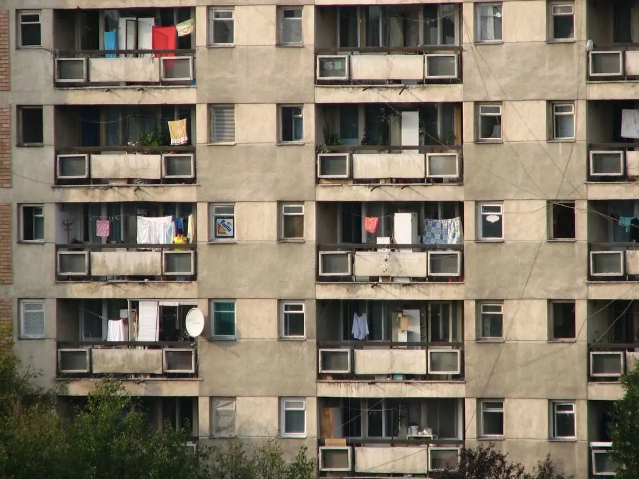 In the image there is a building with walls, windows, balconies and ropes with many clothes. There...