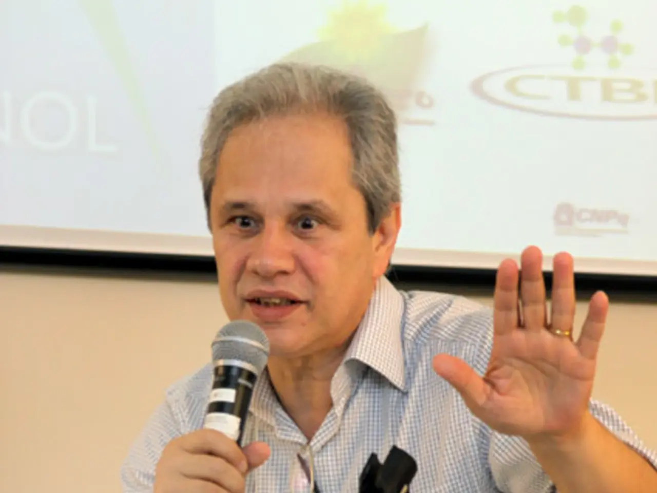 In this image I can see a man is speaking in the microphone, he is wearing the shirt, at the bottom...