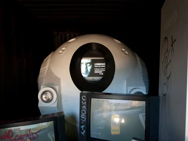 In this picture there is a device and there are two televisions. There is a reflection of trees,...