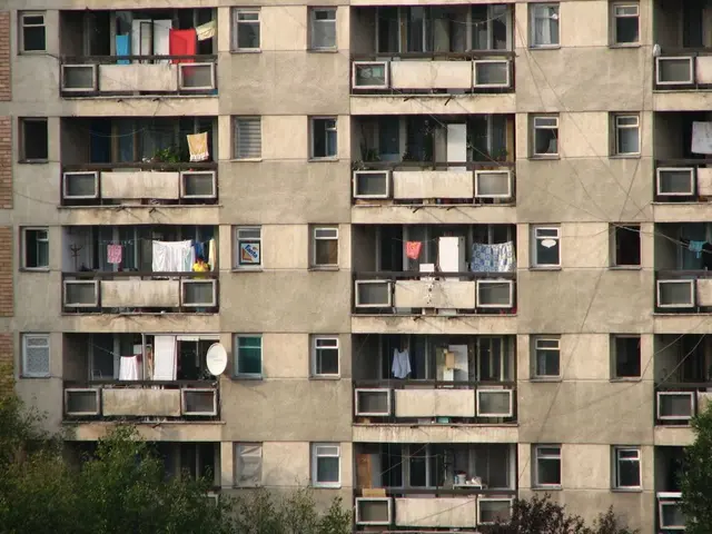 In the image there is a building with walls, windows, balconies and ropes with many clothes. There...