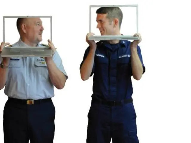 In this image we can see two people standing and holding laptops in their hands.