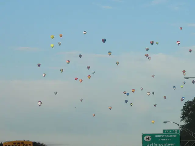 In this image we can see a group of hot air balloons in the sky. On the right side we can see a...