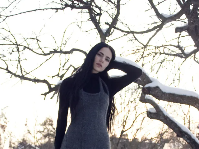 Land is covered with snow. This person is standing. Background there are houses and trees.