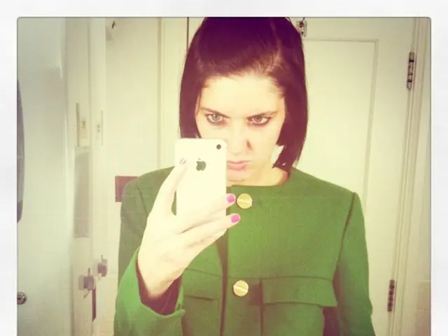 In this picture we can see a woman is holding an iPhone, in the background there is a door, this...