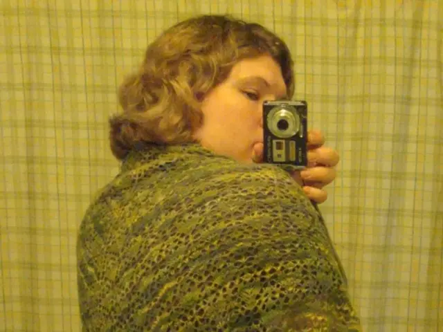 In this image we can see a lady holding a camera and taking a picture, also we can see the cloth.