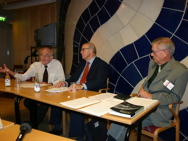 There are three people sitting in chairs in front of table and there are papers.