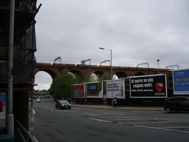 There are few vehicles on the road and there is a bridge in the background and the sky is cloudy.